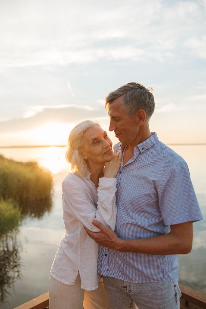 Mature couple embracing at sunset on a wooden pier overlooking water