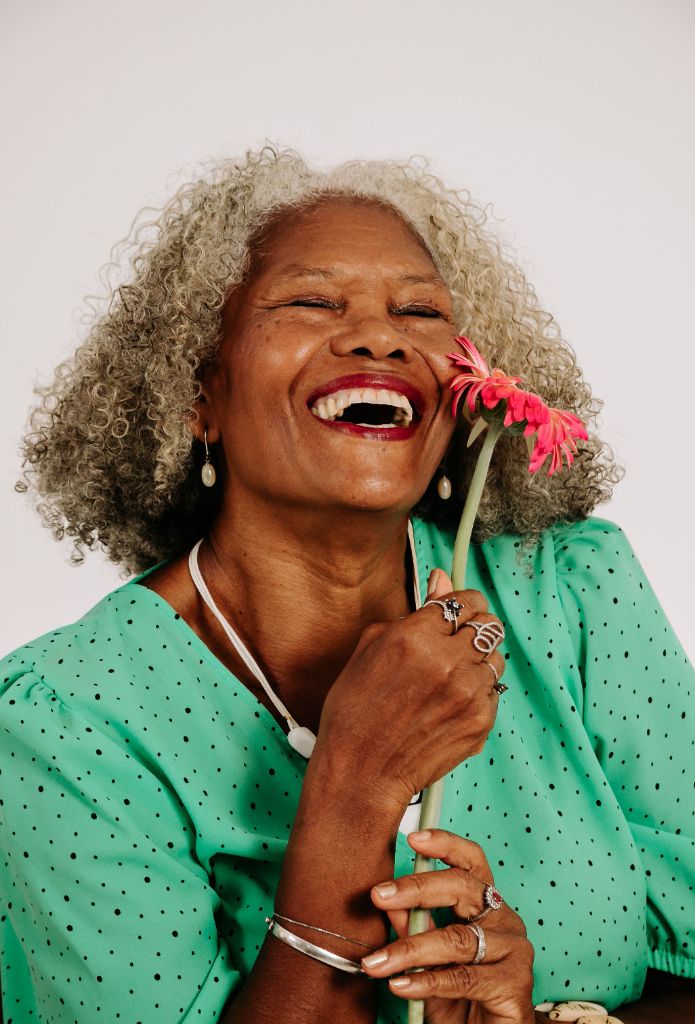 Joyful senior woman with silver curls laughing while holding a pink flower