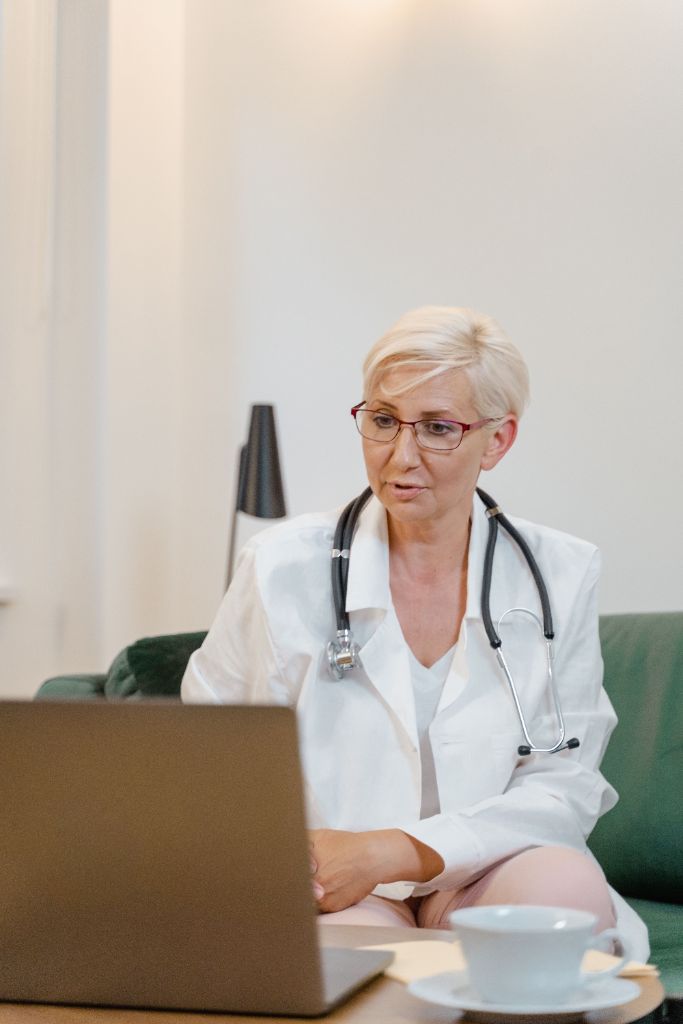 Female clinician with glasses on a video consultation in front of a laptop