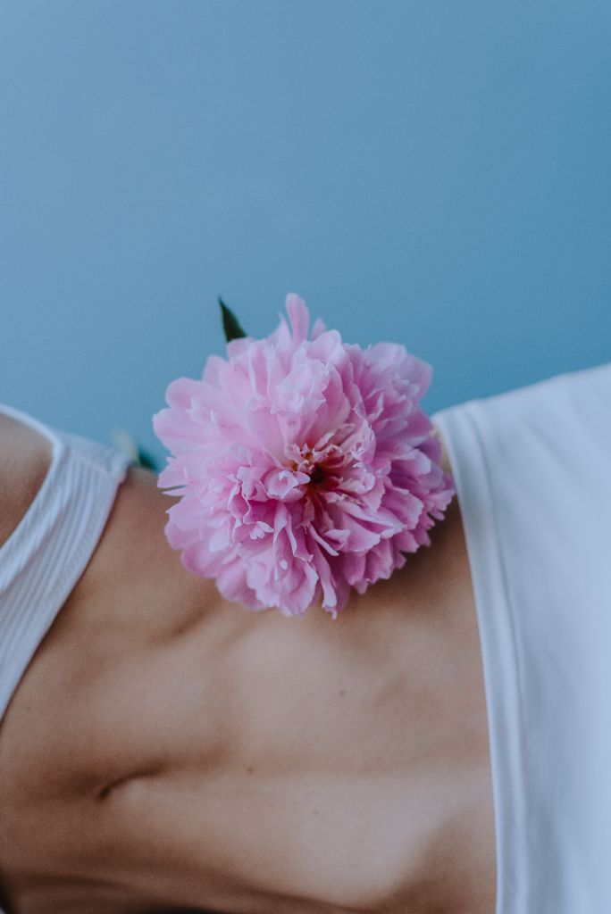 Lush pink flower resting gently against a woman's stomach against a soft blue background