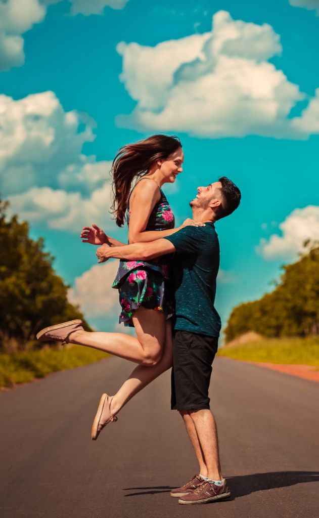 Joyful couple embracing playfully under dramatic bright blue skies with white clouds on an open road